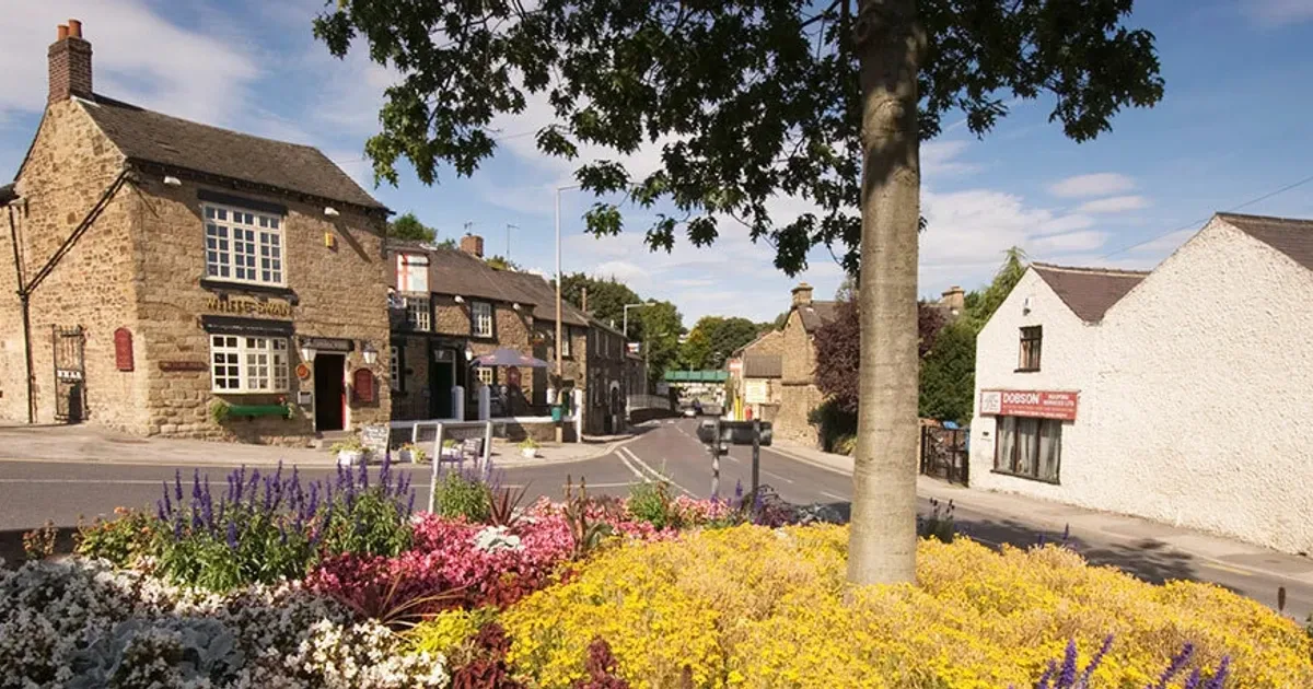A stone pub on a corner in Dronfield, with beds of summer flowers in the foreground and blue sky